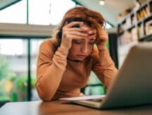 Dejected woman sitting at a table, holding her hands in her head.