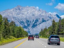 An outstretched road on the Alberta countryside, with a mountain in the background.