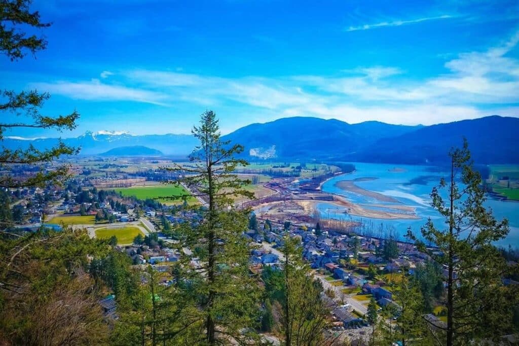 An aerial shot of greenery and homes against the Fraser Riser in British Columbia, with mountains visible in the background.