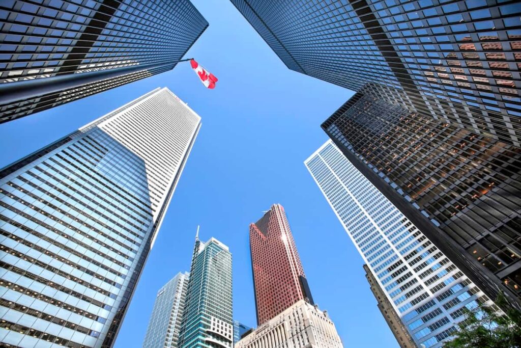 A upward view of the Toronto skyline taken from the ground, with a Canadian flag in the background.