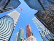 A upward view of the Toronto skyline taken from the ground, with a Canadian flag in the background.