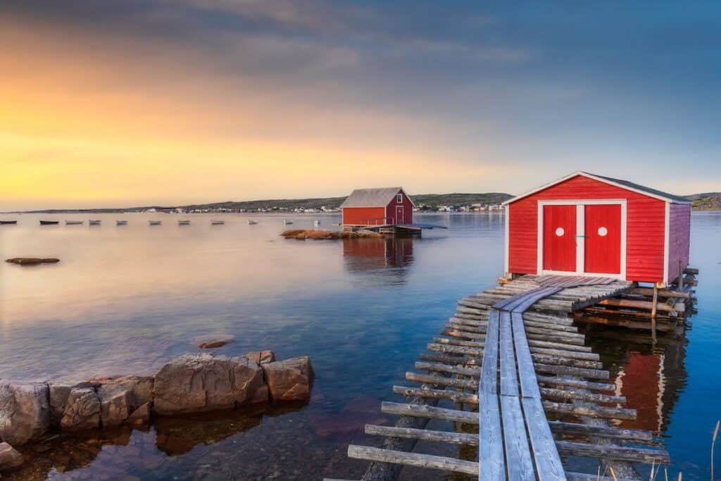 A view of red fishing sheds set up along the water in Newfoundland and Labrador, at sunset.