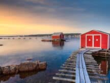 A view of red fishing sheds set up along the water in Newfoundland and Labrador, at sunset.