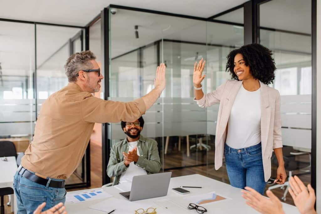Two colleagues giving one another a high-five across a table.