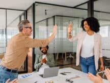 Two colleagues giving one another a high-five across a table.