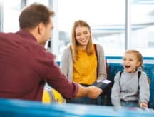 Father handing passport to smiling daughter, which is being held by her mother.