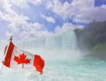 The Canadian flag against Niagara falls on a semi-cloudy day.