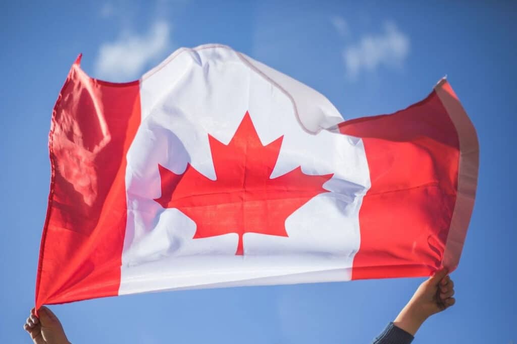 A pair of hands holding a Canadian flag that is waving in the wind, shot with the sky as the backdrop.