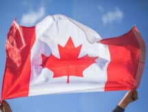 A pair of hands holding a Canadian flag that is waving in the wind, shot with the sky as the backdrop.