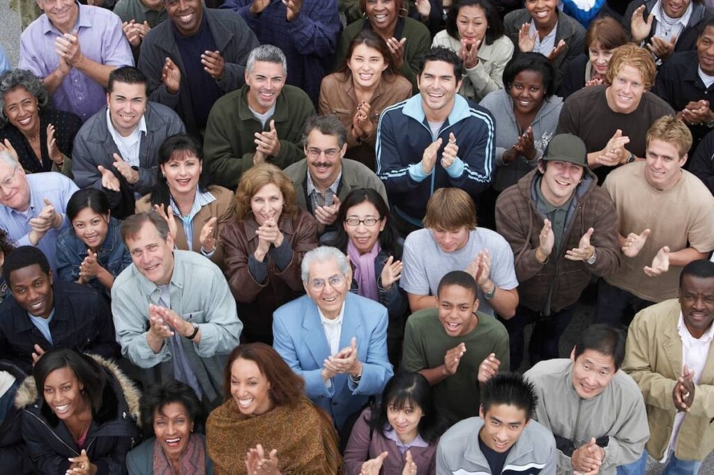 A shot of a big group of diverse people clapping and smiling.