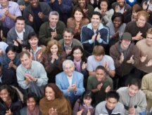 A shot of a big group of diverse people clapping and smiling.
