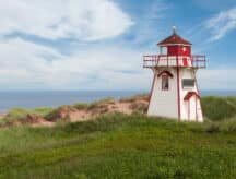 A lighthouse on the PEI coast looks out over the water on a cloudy summer day