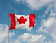 Canadian flag waving in the wind, against a semi-clear blue sky.