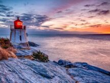 A view of a lighthouse on the Rhode Island coast during a sunset.