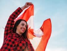 A woman stands outside on a clear day, draped in a Canadian flag
