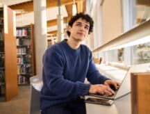 An international student sitting in a library with his laptop