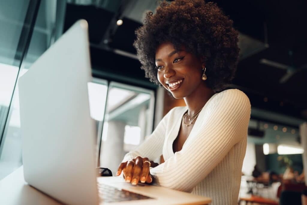 Young woman wearing a white shirt sitting at a table and smiling at her laptop.