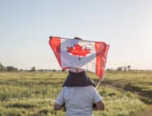 A child raises the Canadian flag while sitting on his father's shoulders.