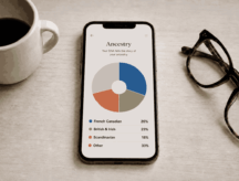 A phone sits atop a coffee table showing ancestry results of its owner, with glasses and a cup of coffee to each side of the frame
