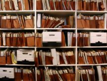 A filling shelf filled with files and organizers, cluttered.