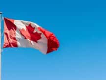 A Canadian flag blows in the wind against a clear blue sky.