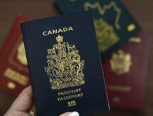 A hand holding a Canadian passport, with other passports in the background.