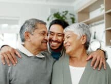 An adult son hugging his mother and father from behind.