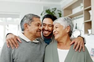 An adult son hugging his mother and father from behind.