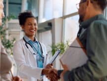 A female doctor shaking hands with a male, both smiling.