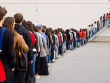 Many people waiting in a long line, to enter a building.