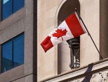 A Canadian flag, hoisted against a beige building.