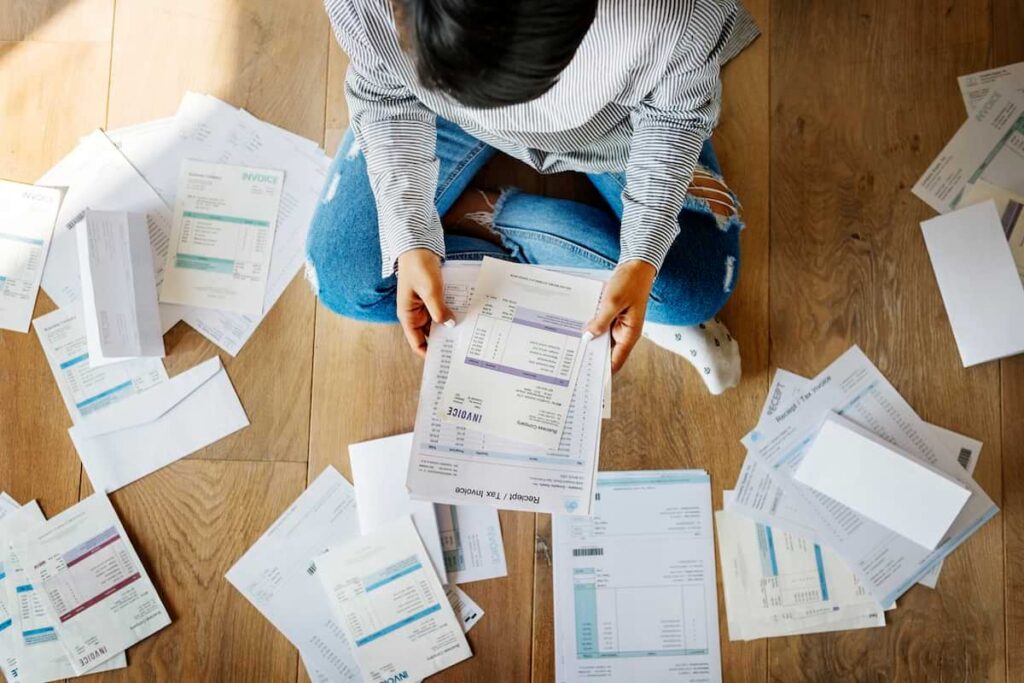 Woman sitting on floor, sorting through heap of financial documents.
