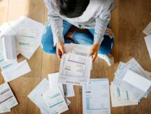 Woman sitting on floor, sorting through heap of financial documents.
