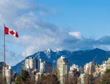 A shot of the Vancouver City skyline, with mountains in the background and a Canadian flag in the foreground.