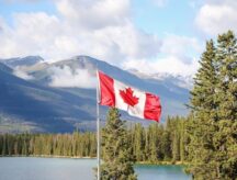 The national flag of Canada against a blue sky in the Canadian Rockies.