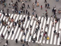 Many people walking across a crosswalk in different directions.