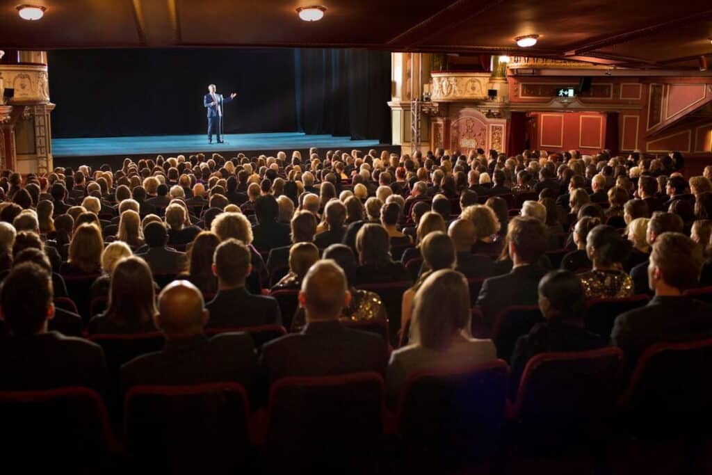 An audience watching a performer on stage in a theater.