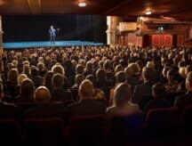 An audience watching a performer on stage in a theater.