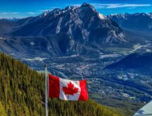 A Canadian flag with a panoramic view of Banff and rocky mountains in the background.