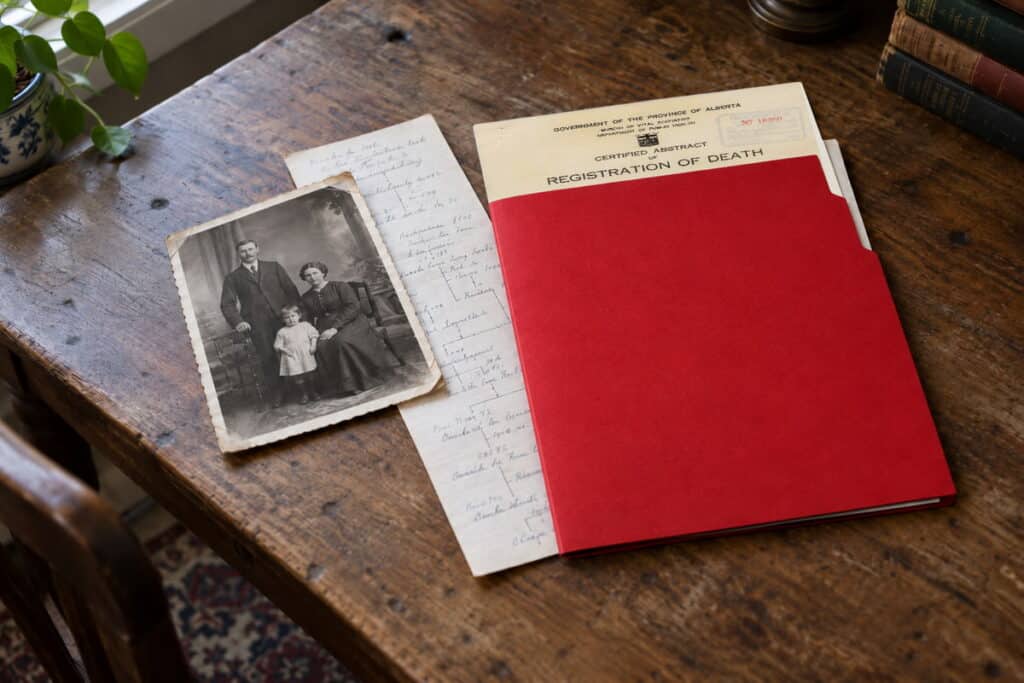 A busy desk showing a picture of Canadian ancestors, a red folder, and a small family tree.