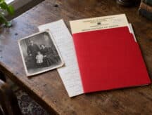 A busy desk showing a picture of Canadian ancestors, a red folder, and a small family tree.
